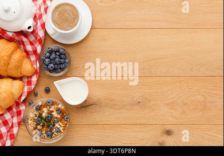 Frühstück auf einem Holztisch mit Kaffee, Croissants, Joghurt und Heidelbeeren Stockfoto