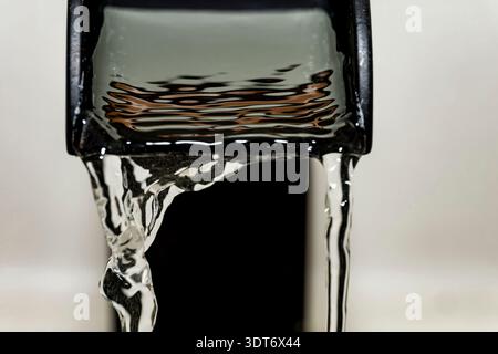 Makroaufnahme von klarem Wasser, das aus einem rechteckigen Auslauf fließt, zeigt Textur, Bewegung und Details der fließenden Oberfläche Stockfoto