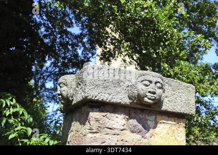 Detaillierte Steinskulptur mit Gesichtern umgeben von Grün, Null Stockfoto