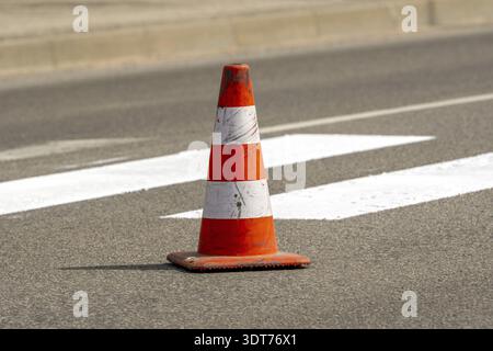 Verkehrskegel mit orangefarbenen und weißen Streifen, der während der Straßenbauarbeiten auf grauem Asphalt auf der Straße steht. Nur weiße Straßenlinien auf Pedes gestrichen Stockfoto