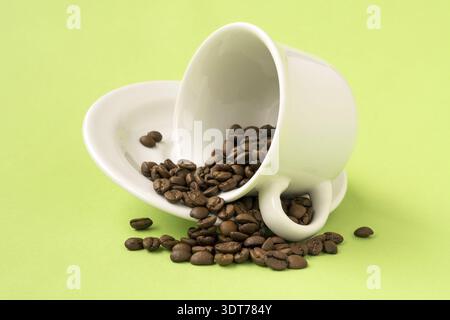 Weiße Tasse gefüllt mit gerösteten Kaffeebohnen fallen auf ein Grüner Hintergrund Stockfoto