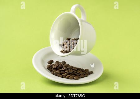 Weiße Tasse gefüllt mit gerösteten Kaffeebohnen, die über einem schweben Grüner Hintergrund Stockfoto