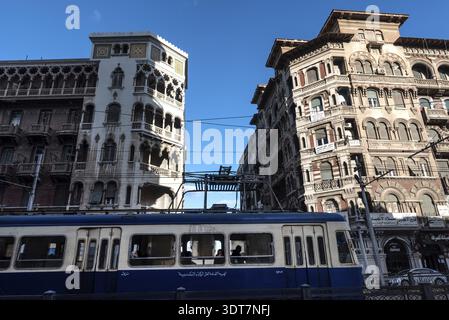 Alexandria, Ägypten. Dezember 2022 historische Architektur und alte Straßenbahn, die in der typischen Alexandria Straße vorbeifährt. Kolonialgeschichte der mediterranen Stadt Stockfoto