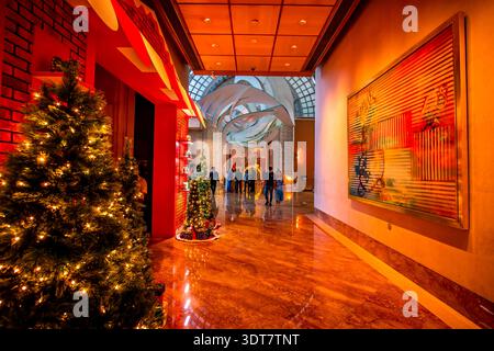 Ein festlicher Weihnachtsbaum beleuchtet die luxuriöse Lobby eines Hotels, während die Gäste durch die warm beleuchtete Halle gehen. Stockfoto