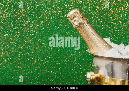 Sektflasche im Eiskübel mit grünem Hintergrund und glitzernder Oberfläche während der Feier Stockfoto