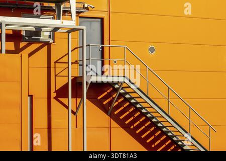 Feuerschutzleiter oder Notausgang mit Stahltreppe an der Wand des orangefarbenen Industriebaus Stockfoto