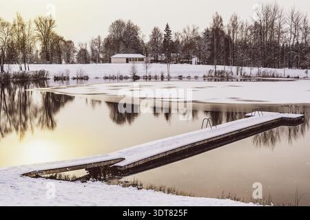 Goldener Sonnenaufgang über einem Steg auf einem gefrorenen Wintersee mit Eis und Schnee Stockfoto