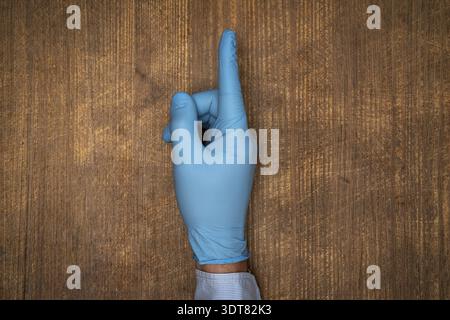 Männliche Ärztin Hand in blauem Handschuh machen Geste mit Zeigefinger nach oben Stockfoto