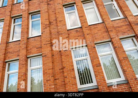 Fassade des Bürogebäudes. Rote Backsteinmauerfragmente mit Wolkenspiegelungen in Fenstern Stockfoto