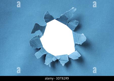 Bahnbrechende Papieröffnung. Zerrissenes blaues Papierblatt mit rundem Loch in der Mitte und weißem Hintergrund Stockfoto