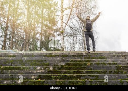 Mann, der oben auf einer moosigen Treppe steht und die Hände hochhebt. Nicht erkennbare Rückansicht Stockfoto