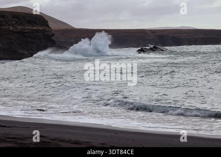 Blick auf den stürmischen Atlantik, während die Wellen gegen den dunklen, steinigen Strand krachen Stockfoto