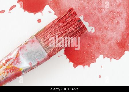 Pinsel und Spritzer von rotem Aquarell. Nahansicht Stockfoto