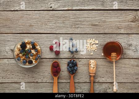 Food Collage mit verschiedenen Beeren, Hafer, Honig und Holzlöffeln auf einem Holztisch Stockfoto