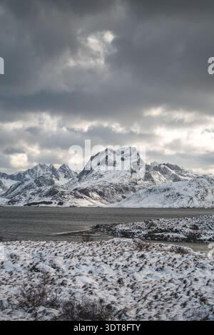 Über einem blauen Fjord auf den Lofoten in Norwegen erheben sich scharfe Gipfel und schneebedeckte Bergrücken, die die raue arktische Schönheit der Winterlandschaft unter hellem Licht einfangen Stockfoto