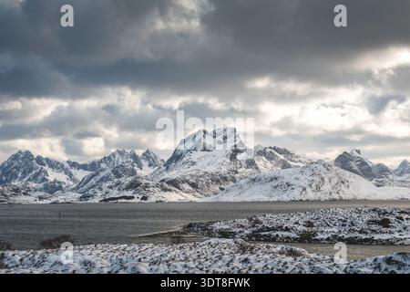 Über einem blauen Fjord auf den Lofoten in Norwegen erheben sich scharfe Gipfel und schneebedeckte Bergrücken, die die raue arktische Schönheit der Winterlandschaft unter hellem Licht einfangen Stockfoto