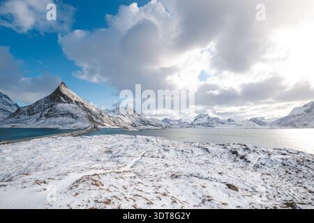 Über einem blauen Fjord auf den Lofoten in Norwegen erheben sich scharfe Gipfel und schneebedeckte Bergrücken, die die raue arktische Schönheit der Winterlandschaft unter hellem Licht einfangen Stockfoto
