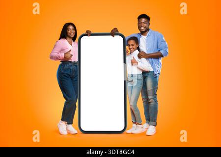 Gruppe von Freunden lächelt und posiert mit einem großen leeren Telefon vor einem orangefarbenen Hintergrund Stockfoto