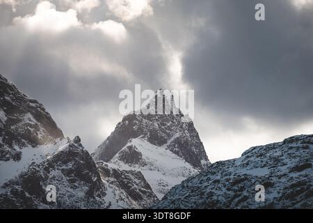 Über einem blauen Fjord auf den Lofoten in Norwegen erheben sich scharfe Gipfel und schneebedeckte Bergrücken, die die raue arktische Schönheit der Winterlandschaft unter hellem Licht einfangen Stockfoto