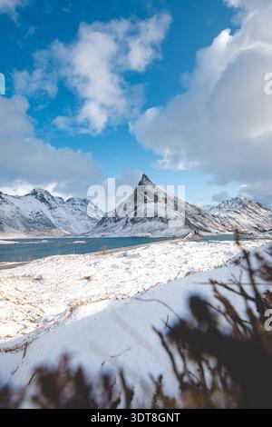 Über einem blauen Fjord auf den Lofoten in Norwegen erheben sich scharfe Gipfel und schneebedeckte Bergrücken, die die raue arktische Schönheit der Winterlandschaft unter hellem Licht einfangen Stockfoto