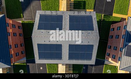 Luftaufnahme von Wohngebäuden mit dunklen Solarpaneelen auf grauen Ziegeldächern, umgeben von grünem Gras und dunklen Asphaltwegen bei Desire by Strata Homes in Leeds, Großbritannien. Stockfoto