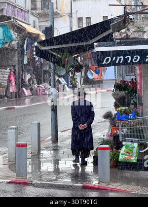 Haifa, Israel, 20. Februar 2026, Rückansicht eines orthodoxen jüdischen Mannes, der bei Regenfällen auf einer nassen Stadtstraße stand. Stockfoto