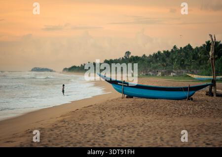 Das traditionelle Sri-lankische Fischerboot Oruwa parkte am Sandstrand bei Sonnenuntergang mit Ozeanhintergrund Stockfoto