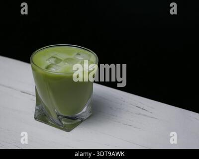 Cremiger Pistazienlikör mit Eiswürfeln in einem kurzen Glas auf weißem Tisch und schwarzem Hintergrund. Elegantes Alkoholgetränk-Konzept mit Kopierraum. Stockfoto