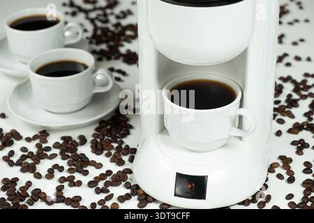 Weiße Kaffeemaschine mit einer vollen Tasse frischen Kaffee und verstreuten Bohnen Stockfoto