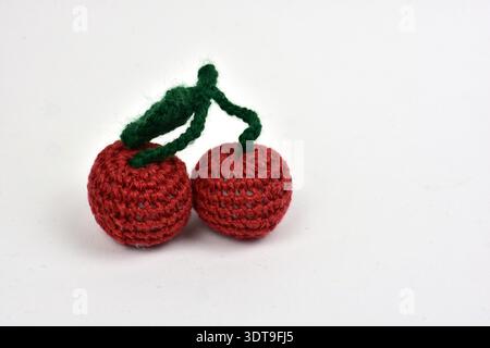 Handgemachte rote Kirschen, isoliert auf weißem Hintergrund. Gestricktes Fruchtspielzeug mit grünem Stiel und detaillierter Garnstruktur, minimaler Studiofotografie. Stockfoto