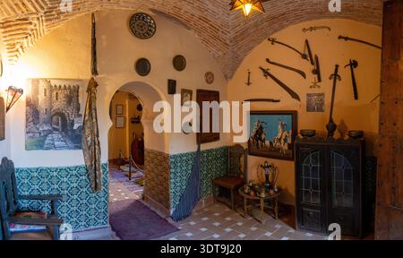 Caceres, Spanien - 25. November 23: Großer Blick auf einen historischen Museumsraum mit maurischem Bogen, an der Wand montierten Schwertern, kunstvollem Dekor und einer Wasserpfeife im Các Stockfoto