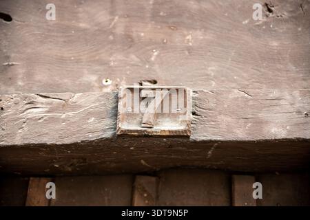 Rustikales Metallhaus Nummer sieben auf einem verwitterten Holzbalken montiert, mit Patina und abgenutzter Farbe, eine Vintage-Türtafel, die an Nostalgie erinnert, Handwerker Stockfoto