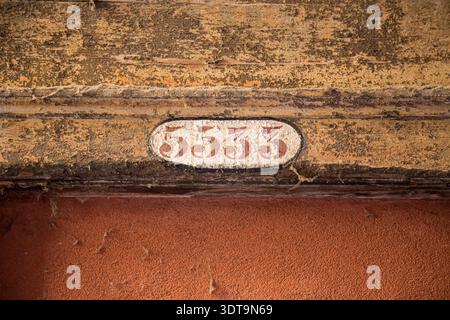 Nahaufnahme einer Vintage-Hausnummer-Plakette mit der Aufschrift 5533, die auf einer verwitterten, strukturierten Wand über einer Tür angebracht ist und abblätternde Farbe, Patina und rustikale Farbe zeigt Stockfoto