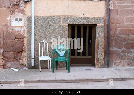 Leerer grüner Plastikstuhl vor einem lokalen Haus in Azofra La Rioja Spanien mit gebrochener Gipswand und alter Tür am Camino Juli 2024 Stockfoto