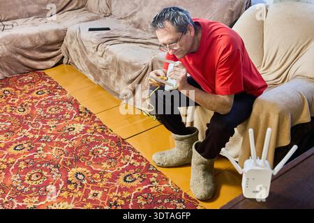 Ein älterer Mann passt den Router für die wlan-Signalverteilung im Landhaus an. Stockfoto