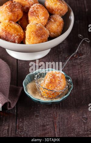 Zuckerbeschichtete Donuts mit Likör und Wein auf rustikalem Tisch, gemütliche Dessertszene im Stillleben. Stockfoto