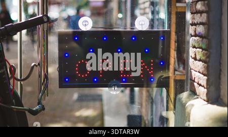 Helles offenes LED-Schild mit roten und blauen Lampen, sichtbar in einem Schaufenster Stockfoto