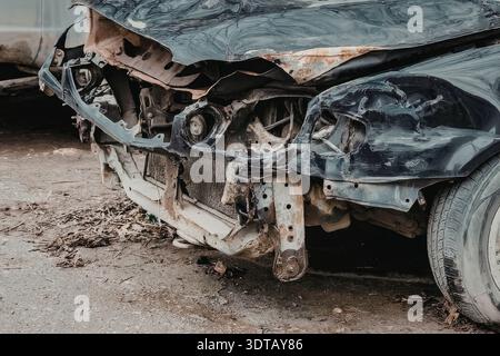 Das Bild zeigt eine Nahaufnahme einer beschädigten Fahrzeugfront mit einer zerknitterten Motorhaube, defekten Scheinwerfern und einem verbeulten Stoßfänger, was auf einen schweren Unfall hinweist. Stockfoto