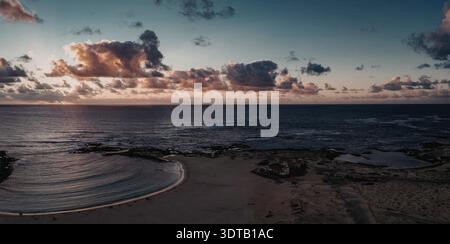 Eine ruhige Strandszene bei Sonnenuntergang mit sanften Wellen und einem lebendigen Himmel Stockfoto