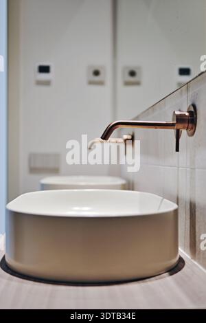 Modernes Badezimmer mit zwei weißen runden Waschbecken auf der Arbeitsplatte und minimalistischen, an der Wand montierten Kupferarmaturen Stockfoto