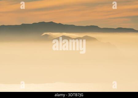 Weicher Nebel und glühender Ozean unter geschichteten Bergsilhouetten über dem Wolkenmeer bei Sonnenuntergang, Blick vom Teide-Krater in Richtung La Gomera, Teneriffa Stockfoto