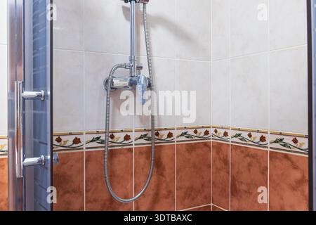 Nahaufnahme eines modernen Duschkopfs und Wasserhahns an einer gefliesten Wand mit dekorativer Borte und einer Glasduschtür Stockfoto