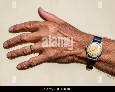 Ein älterer Mann Hand mit einer Vintage Armbanduhr mit schwarzem Lederarmband. Die Textur der Hand zeigt das Alter, mit sichtbaren Falten und Venen, was darauf hindeutet Stockfoto