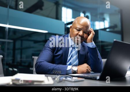 Gelangweilter schwarzer Geschäftsmann, der im Büro am Laptop arbeitete Stockfoto