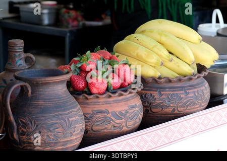Bunte Schüsseln mit Erdbeeren und Bananen ruhen auf einem Tisch auf einem lebhaften Markt. Stockfoto
