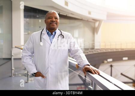 Reifer schwarzer Geschäftsmann, der mit selbstbewusstem Lächeln auf dem Balkon des Klinikbüros steht Stockfoto