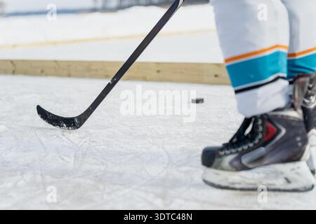 Eishockeyausrüstung in Aktion, schwarzer Stick, der auf der gefrorenen Eisbahn nach Puck greift, während der Spieler vorbeigleitet, Sportbewegung und Übungskonzept aus nächster Nähe Stockfoto