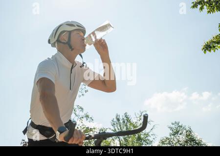 Radfahrer trinken Wasser aus der Flasche während der Fahrt an sonnigen Tagen Stockfoto