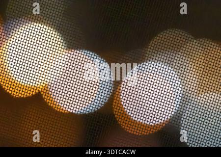 Warme und kühle runde Bokeh-Lichter, die durch ein dunkles Gitter aus Metall leuchten, erzeugen ein geometrisches Muster aus verschwommenen Kreisen mit Kopierraum für minimales digi Stockfoto