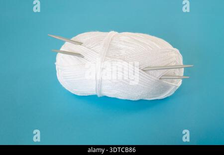 Ein neuer Knäuel aus weißem Garn mit einem Paar Stricknadeln. Stockfoto